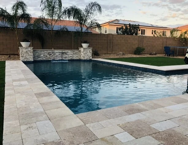 Rectangular Phoenix pool with a stone water-feature wall and travertine deck at dusk